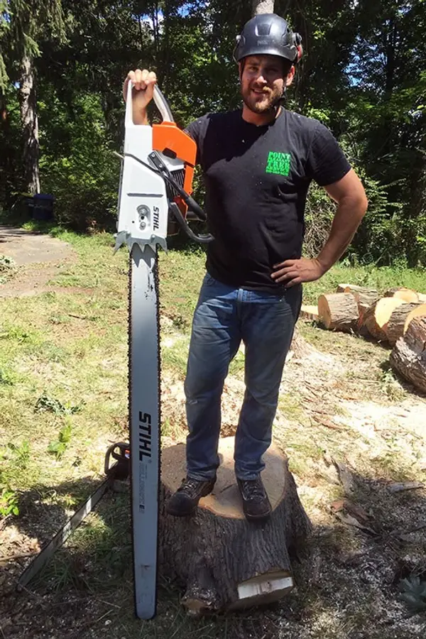 Mike Langer, owner of Point Pleasant Tree Service, standing on a fresh stump with a large chainsaw