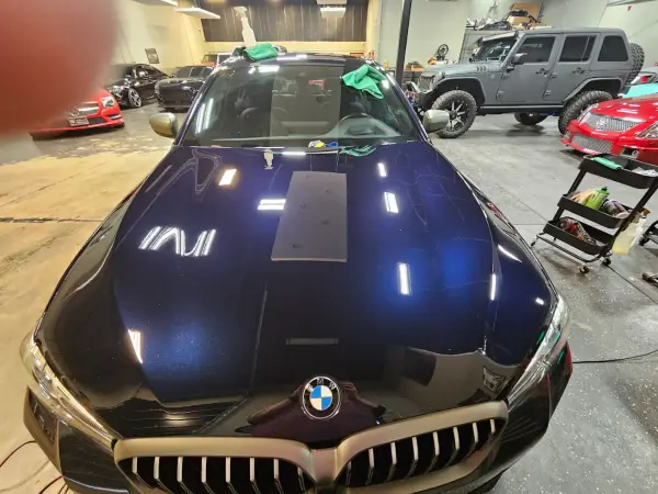 Black BMW hood under detailing lights during paint-correction work at JRC Shine