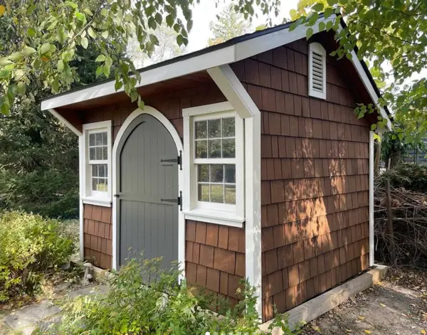 Brown cedar-shake shed with white trim, a gray arched door, and white window casings