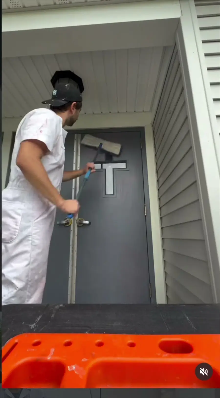Painter in white coveralls sanding the top of a gray exterior door under a porch